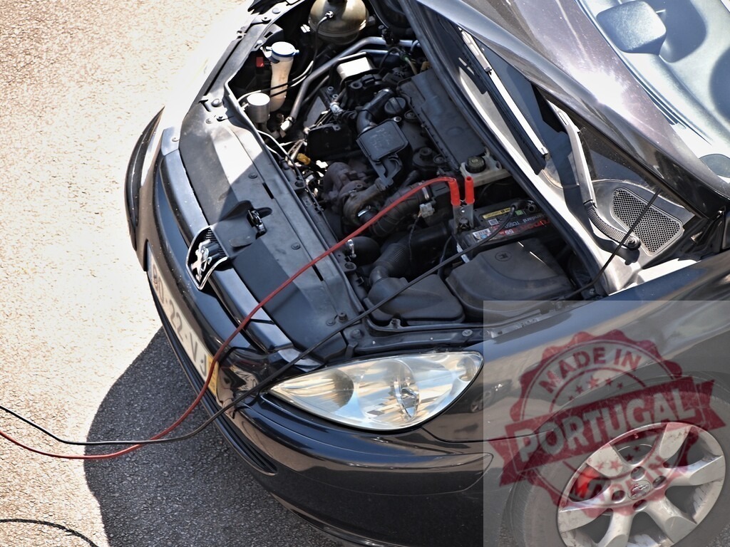 Peugeot car with open hood jump starting battery | Car undergoing a jump start with jumper cables connected to a dead battery - Realized with Pictrs.com