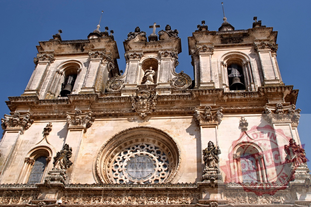Alcobaça Monastery facade showing Baroque and Gothic architecture | Alcobaça Monastery showing its historic facade with intricate architectural details against a clear blue sky - Realized with Pictrs.com