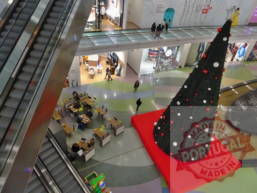 Shopping mall interior with Christmas tree and escalators | Shopping mall interior decorated for Christmas, featuring a large tree, escalators, and people moving through the retail space - Realisiert mit Pictrs.com