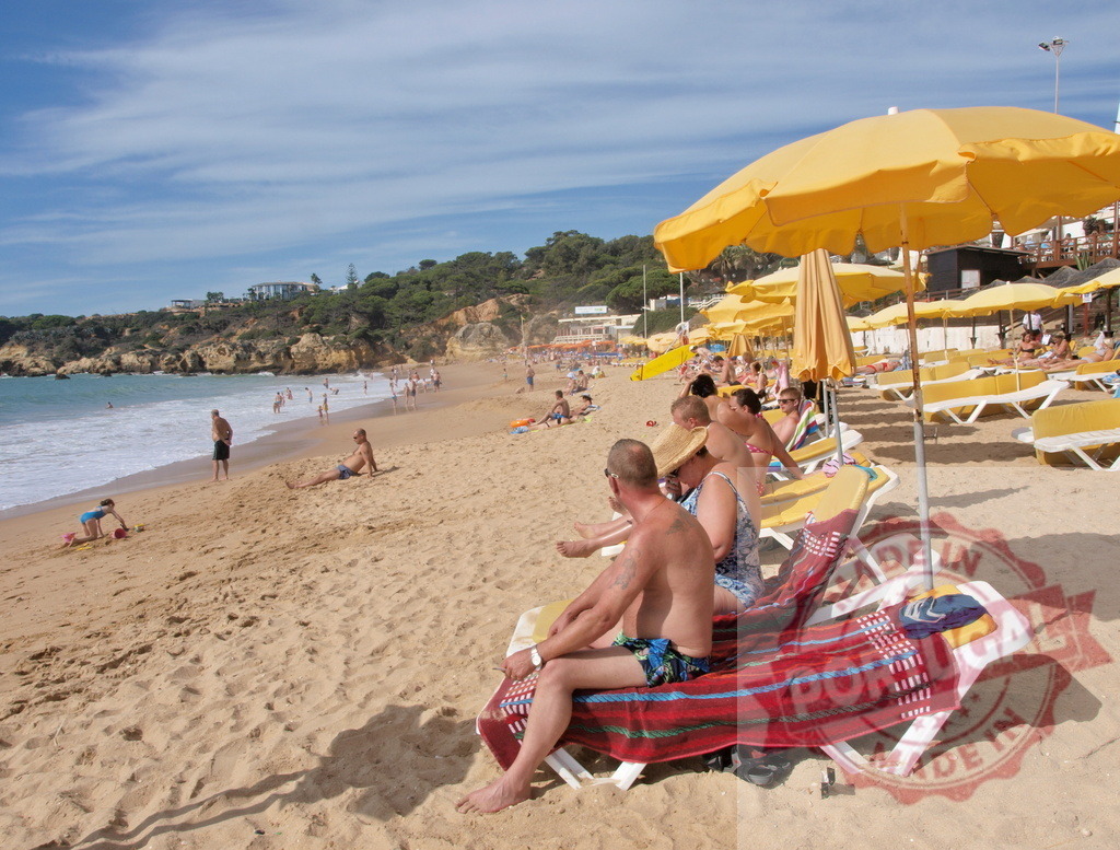 Beachgoers relaxing under yellow umbrellas on a sandy beach | People enjoying a sunny day on a sandy beach with yellow sun umbrellas and turquoise water - Realized with Pictrs.com