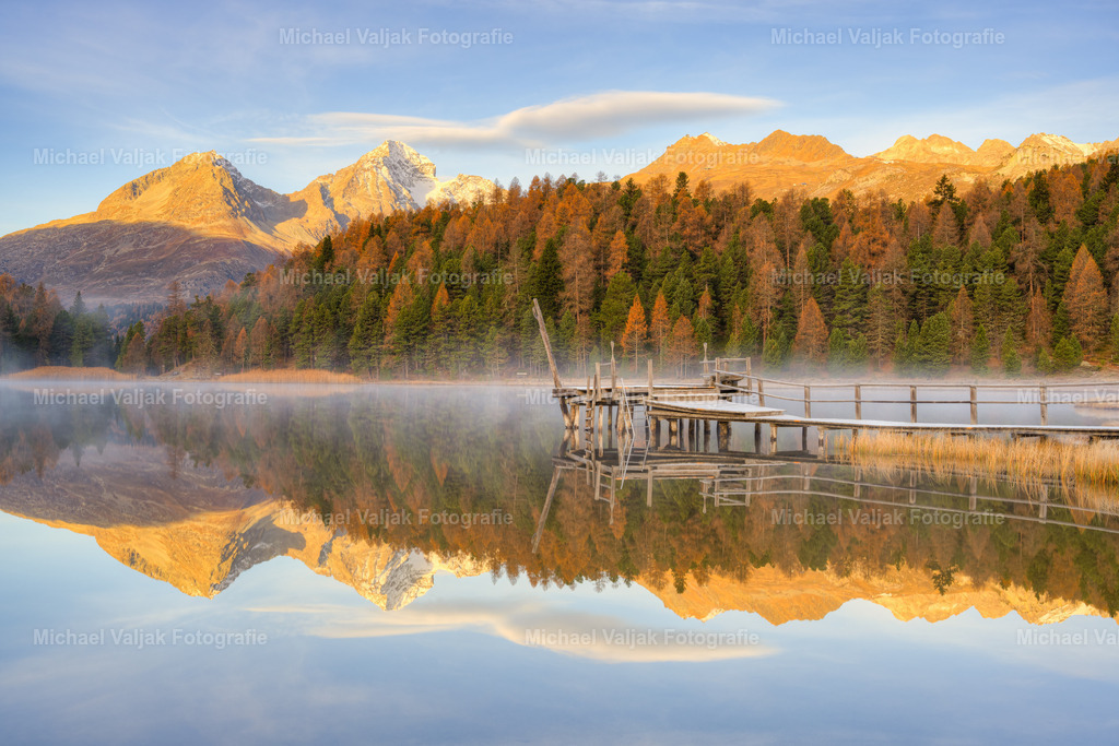 Morgens am Stazersee im Engadin | Frühmorgens am Stazersee bei St. Moritz im Engadin. Die aufgehende Sonne bringt die Berggipfel zum Glühen, leichte Nebelschwaden wabern über den See. Das Wasser ist so ruhig und glatt, dass es eine perfekte Spiegelung gibt.  - Realisiert mit Pictrs.com