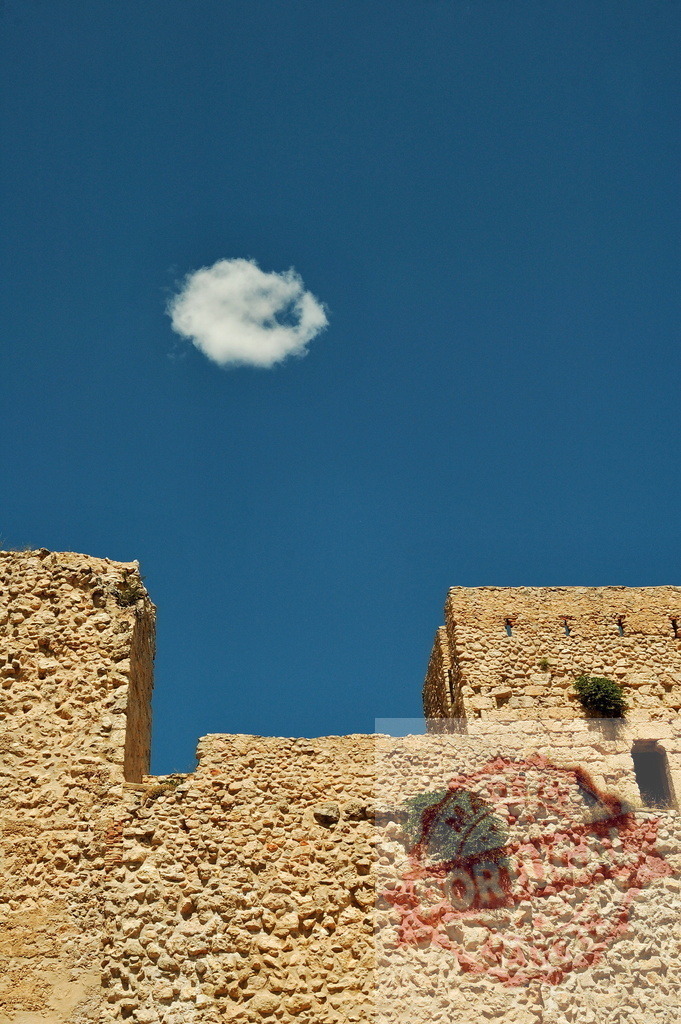 Ancient fortress wall standing under minimalist blue sky | Stone fortress wall details under a clear blue sky with a single white cloud - Realized with Pictrs.com