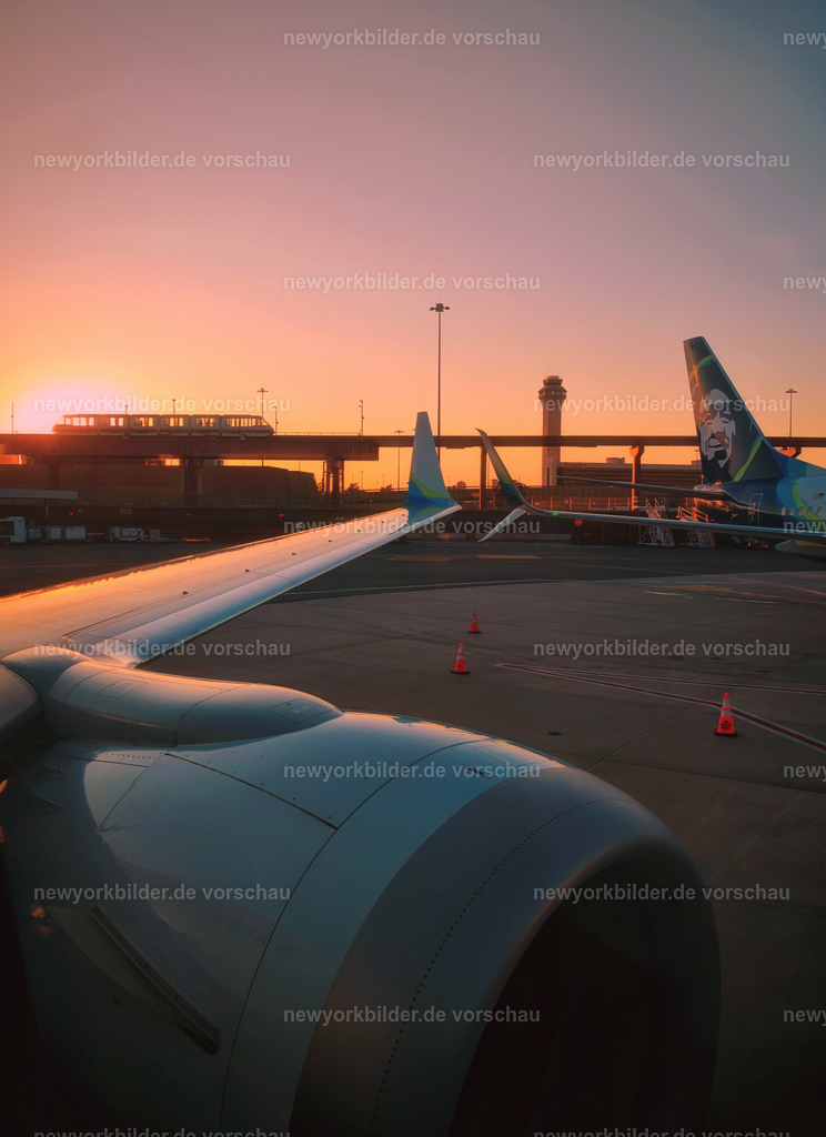 Goldene Stunde am New Yorker Flughafen – Magischer Sonnenuntergang mit AirTrain | Es gibt Momente, die bleiben für immer – und dieser Sonnenuntergang am New Yorker Flughafen gehört dazu. Die goldene Stunde taucht die Szenerie in ein warmes, intensives Orange, das den Himmel wie ein Gemälde erscheinen lässt. Im Hintergrund zieht der AirTrain seine Linie, kontrastreich beleuchtet von den letzten Strahlen der untergehenden Sonne. Die Atmosphäre ist magisch: Stille mischt sich mit der leisen Betriebsamkeit des Flughafens, während die Sonne langsam hinter den Gebäuden verschwindet. Für mich war es ein Augenblick des Innehaltens, bevor die Reise weiterging – von New York nach Los Angeles. Dieses Bild erzählt von Abschied und Vorfreude, von der Schönheit, die selbst in Übergängen liegt. Es ist ein Porträt der Stadt aus einer Perspektive, die man selten sieht: nicht die Skyline, sondern die flüchtige Poesie eines Abends, eingefangen zwischen Himmel und Asphalt. Wer die Magie der goldenen Stunde liebt, findet hier einen Moment purer Inspiration.