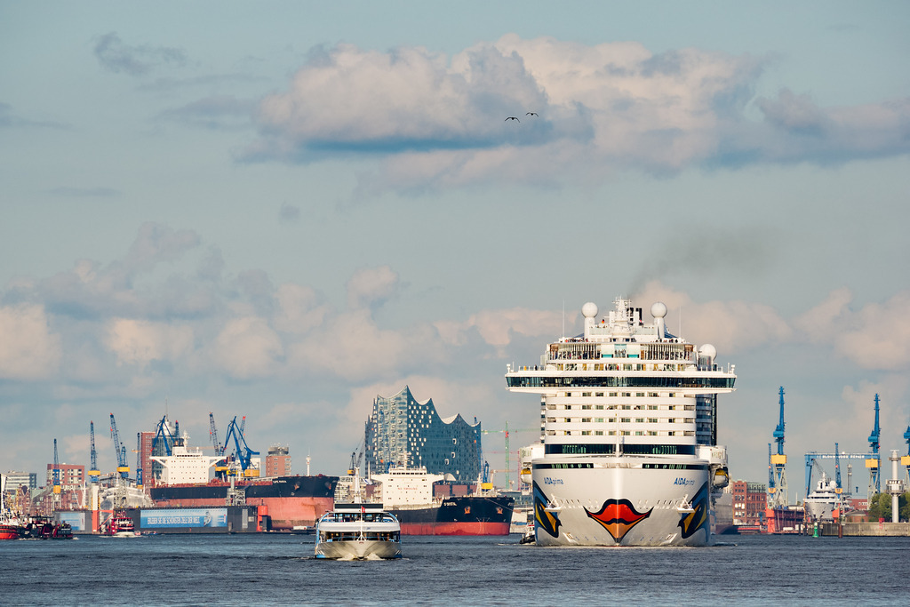 AIDAprima | Bei der Ausfahrt aus dem Hafen Hamburg, das Kreuzfahrtschiff AIDAprima vor der beeindruckenden Hafenkulisse. Das Schiff ist 300 Meter lang, es wurde im Jahr 2014 gebaut. - Realisiert mit Pictrs.com
