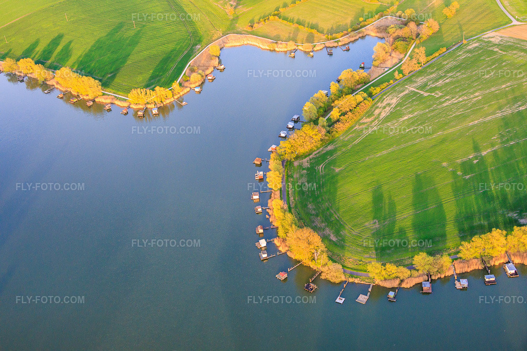 Aerial view: Boardwalks with fishing huts line the shore of Lake Etang du Welschhof. in Puttelange-aux-Lacs in the state Moselle, France. – Photo: IMG_154401.jpg taken on 04/17/2026 by Werner Riehm/FLY-FOTO.com – Resolution of the original: 6000 x 4000 px
