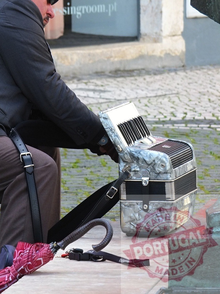 Man busking with accordion playing street music outdoors | Man playing accordion as a street musician on cobblestone pavement with an umbrella - Realisiert mit Pictrs.com