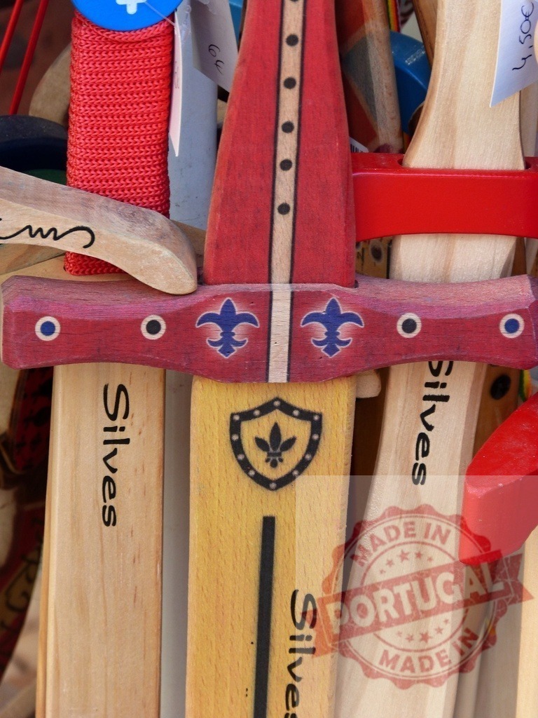 Wooden toy swords with fleur-de-lis and Silves branding | Wooden toy swords displayed for sale at an outdoor market, featuring heraldic details - Realisiert mit Pictrs.com