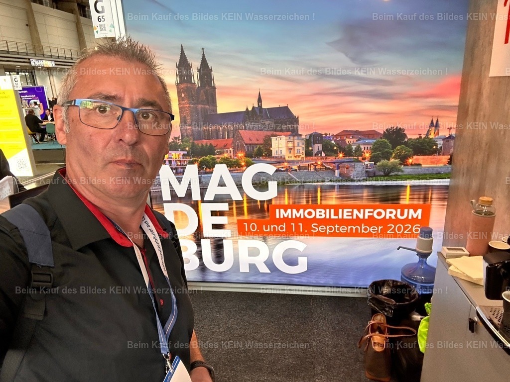 115_Messe_real_estate_real_estate_0382 | Ein besonderer Moment in Hannover --- Dieses Selfie entstand auf der Immobilienmesse Real Estate in Hannover am Gemeinschaftsstand der Landeshauptstadt Magdeburg. Eigentlich ist es nur ein einfaches Handyfoto – und trotzdem bedeutet es mir sehr viel.--- Direkt hinter mir, außerhalb des Bildes, befand sich der Stand der Investitions- und Marketinggesellschaft Sachsen-Anhalt. Dort entdeckte ich zahlreiche meiner Luftbilder, die ich ein Jahr zuvor im Auftrag für das Standortmarketing fotografiert hatte. In diesem Moment wurde mir bewusst, welchen Weg meine Arbeit inzwischen genommen hatte. Meine Luftbilder waren nicht mehr nur Fotografien für Kalender oder Ausstellungen. Sie wurden genutzt, um Sachsen-Anhalt auf einer der wichtigsten Immobilienmessen Europas zu präsentieren. Darauf war ich schon ein wenig stolz. PUNKT - Realisiert mit Pictrs.com