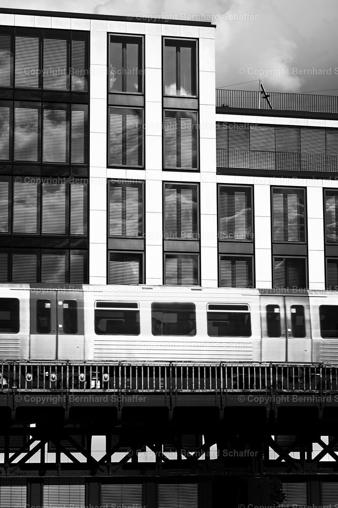 Metro in der City | Die Vorbeifahrt eines Metro Zuges an einem Gewerbekomplex in Hamburg / Deutschland, schwarz-weiss. - Realisiert mit Pictrs.com