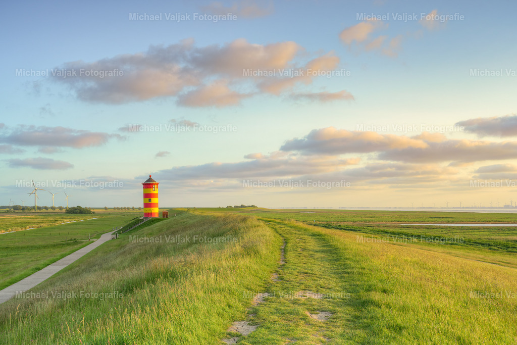 Auf dem Deich beim Pilsumer Leuchtturm in Ostfriesland | Blick entlang des Deiches zum Pilsumer Leuchtturm. Der Leuchtturm ist ein Wahrzeichen Ostfrieslands und vor allem aus dem Film "Otto - der Außerfriesische" bekannt. Er ist dadurch einer der bekanntesten Leuchttürme Deutschlands.Der Turm weist eine leichte Schieflage nach Osten auf (im Bild links). Im Laufe der Jahrzehnte hat er sich durch den oft starken Wind in diese Schräglage begeben, da das Fundament selbst nicht auf Stützen steht. Es handelt sich hierbei also nicht um einen Bildfehler. - Realisiert mit Pictrs.com