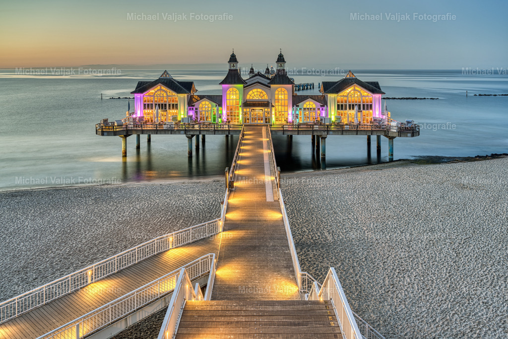 Seebrücke in Sellin auf Rügen am Abend | Jeden Abend wird die berühmte Seebrücke in Sellin auf Rügen sowie der Weg dorthin mit zahlreichen Scheinwerfern angeleuchtet. Die Gebäude der Seebrücke werden zusätzlich mit bunten Scheinwerfern in Szene gesetzt. Ein toller Anblick und eins der schönsten Ostseemotive wie ich finde.  - Realisiert mit Pictrs.com