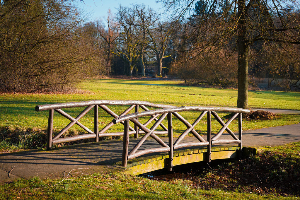 Brücke - Bad Salzhausen | Ein Bauwerk wie diese Brücke, das sich perfekt in die Landschaft einfügt, komplementiert die Szenerie einer Parkanlage perfekt. Der Kurpark in Bad Salzhausen ist vor allem für die mineralischen Quellen, das Gradierwerk und die Mühle der ehemaligen Salzsieder bekannt. Doch auch Abseits dieser Wasserattraktionen finden sich kleine und große Kunstwerke, die auch Stammgäste noch überraschen können. Man muss lediglich die angelegten Pfade mit wachem Auge begehen und als Lohn eröffnet sich eine neue Perspektive auf die grüne Kuranlage. - Realisiert mit Pictrs.com