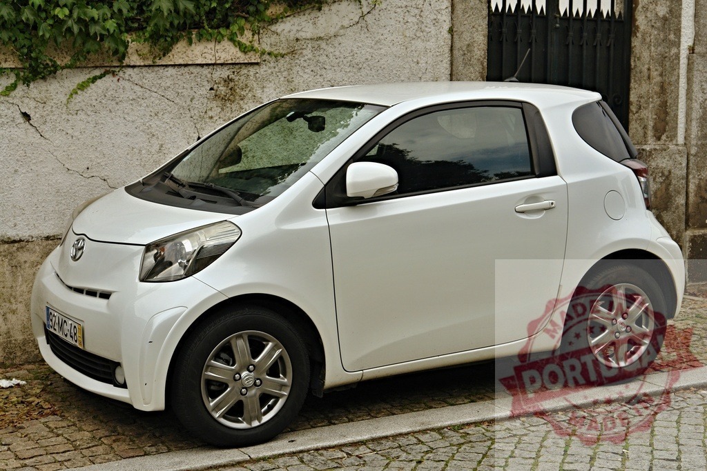 Toyota iQ white compact car parked on street | Toyota iQ, a white compact car, parked on a cobbled stone city street - Realized with Pictrs.com