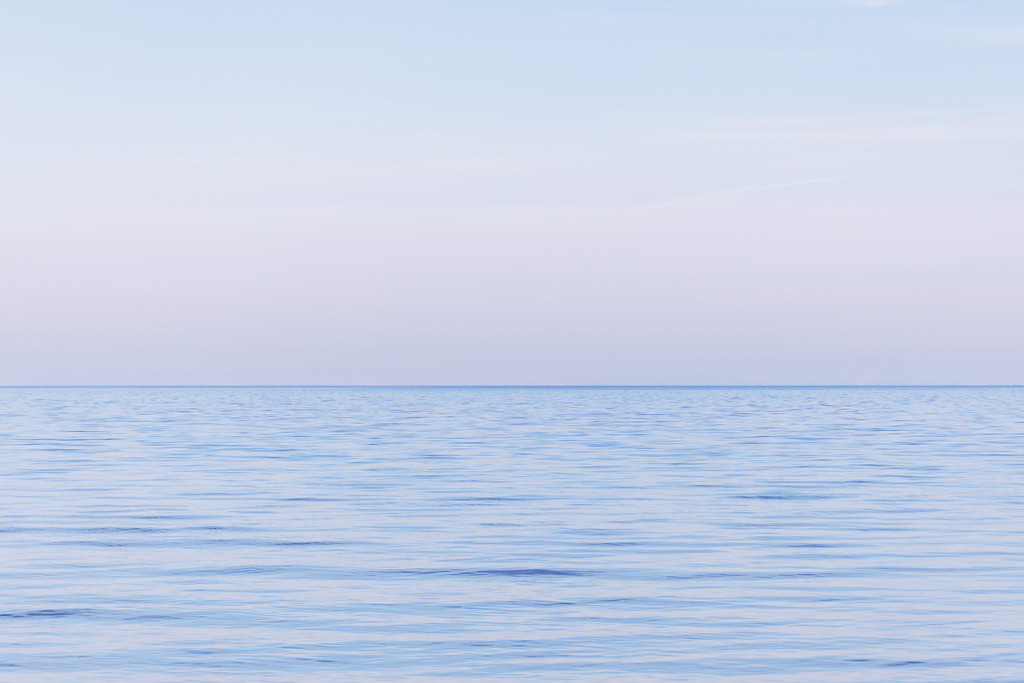 Pastellhimmel über ruhigem Meer – Minimalistische Meeresfotografie | Das stille Meer trifft auf einen zarten Pastellhimmel, dessen weiche Farbverläufe dem Motiv eine besonders sanfte und poetische Ausstrahlung verleihen. Die klare Horizontlinie und die feinen Wellenstrukturen erzeugen eine ruhige Spannung, die das Bild zugleich beruhigend und visuell weit öffnend wirken lässt. Die minimalistische Darstellung betont die Harmonie zwischen Wasser und Himmel und schafft eine Atmosphäre, die moderne Räume mit Leichtigkeit und Eleganz erfüllt. Dieses Fine‑Art‑Wandbild setzt einen dezenten, hochwertigen Akzent und eignet sich ideal für Interiors, die Ruhe, Klarheit und eine subtile ästhetische Tiefe suchen.
