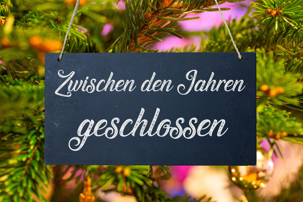 ZWISCHEN DEN JAHREN GESCHLOSSEN  | Betriebsferien an Weihnachten: Schild mit der Aufschrift ZWISCHEN DEN JAHREN GESCHLOSSEN vor einem Weihnachtsbaum - Realisiert mit Pictrs.com