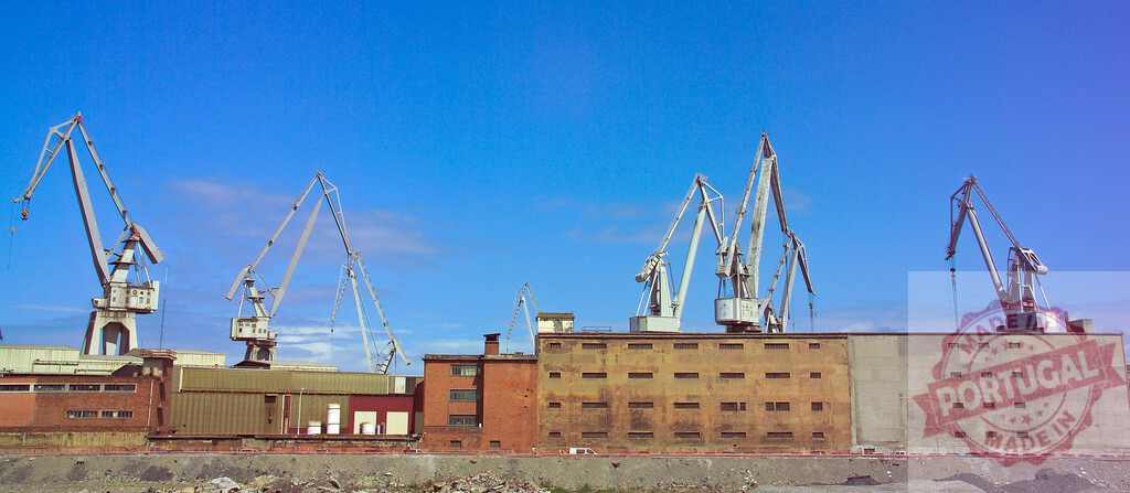 Gantry cranes standing in industrial port against blue sky. Spain - Bilbao | Industrial gantry cranes standing over warehouses at a commercial port during the day - Realisiert mit Pictrs.com