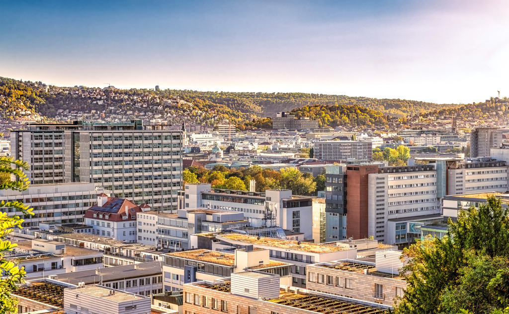Panorama Ansicht der Landeshauptstadt Stuttgart,Weinberge,Talkessel | Das Bild zeigt eine Panoramaansicht der Stadt Stuttgart, der Hauptstadt des Landes Baden-Württemberg in Deutschland. Die Stadt liegt in einem Talkessel, umgeben von Hügeln und Weinbergen.Die Architektur im Bild umfasst moderne Krankenhausgebäude und städtische Strukturen.Die Szene fängt die dichte Bebauung der Stadt inmitten der natürlichen Topographie ein.Es ist ein malerischer Blick auf die facettenreiche Landeshauptstadt. - Realisiert mit Pictrs.com