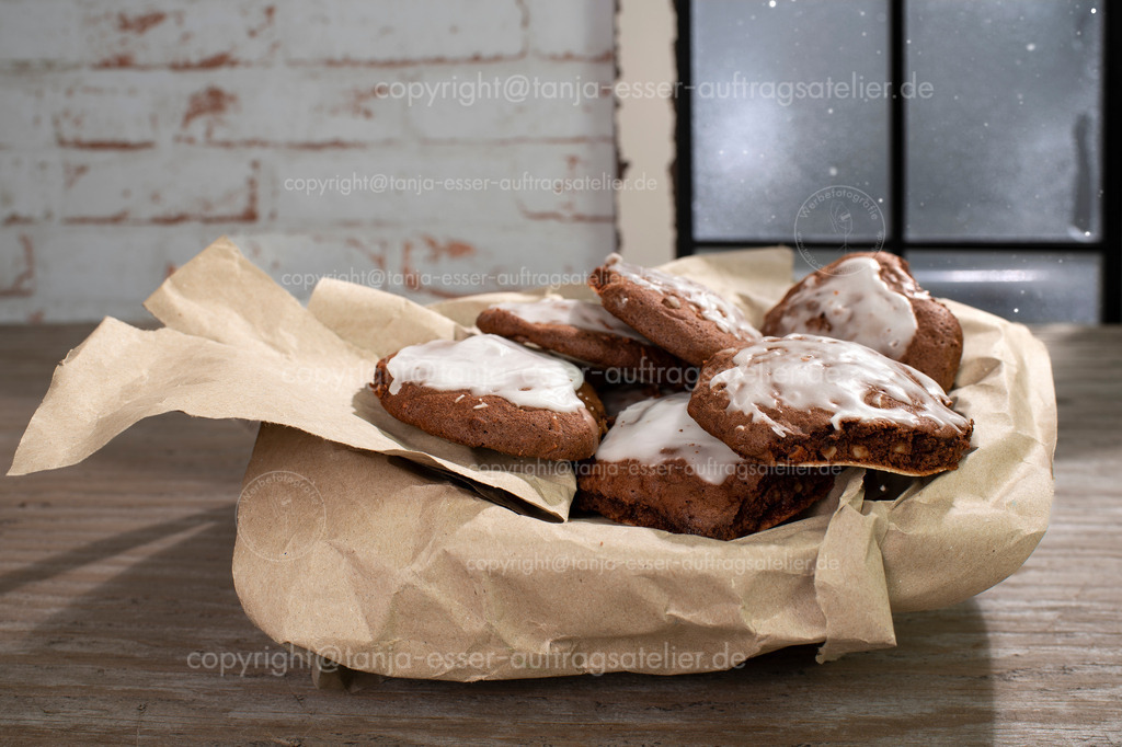 Plaetzch Berliner Brot Packpapier D | Hausgemachte Lebkuchenplätzchen mit Mandeln und Zuckerguss (Berliner Brot) liegen auf Packpapier. Im Hintergrund ist ein vereistes Fenster.