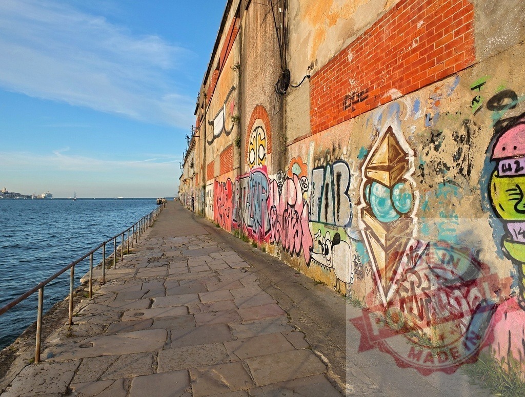 Seaside urban walkway with colorful graffiti art | Coastal walkway featuring an old building wall covered with vibrant graffiti art under a clear blue sky - Realisiert mit Pictrs.com