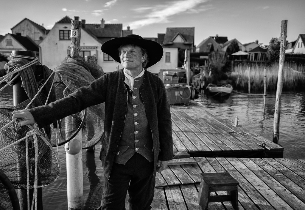 fischer-2020-087 | Jörg Nadler ist Mitglied der Holmer Fischerzunft in Schleswig. Er nennt sich "historischer Fischer", weil er neben seinem Hauptberuf das Fischerhandwerk früherer Epochen als Darsteller u. a. bei museumspädagogischen Veranstaltungen lebendig vermittelt. Hier ist er als Fischer der Barockzeit auf seiner Brücke am Ufer des Holms zu sehen. - Realisiert mit Pictrs.com