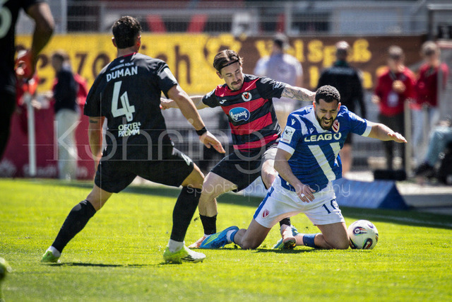 German 3rd Division, Viktoria Koeln vs. Energie Cottbus, 26.04.2026 | KOELN, GERMANY - APRIL 26, 2026:  Simon Handle (FC Viktoria Koeln, 7) fouls Tolcay Cigerci (Energie Cottbus, 10), on the left Taylan Duman (FC Viktoria Koeln, 4) during the 3rd division match on gameday 35 between Viktoria Koeln vs. Energie Cottbus at the Sportpark Hoehenberg on April 26, 2026 in Koeln, Germany. DFL REGULATIONS PROHIBIT ANY USE OF PHOTOGRAPHS AS IMAGE SEQUENCES AND/OR QUASI-VIDEO.
