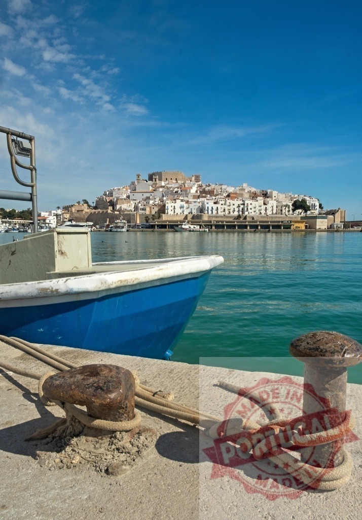 Fishing boat moored in Peñíscola harbor with the skyline in the background | Traditional fishing boat moored at the concrete pier in Peñíscola, Spain, with the old town skyline in the background - Realized with Pictrs.com