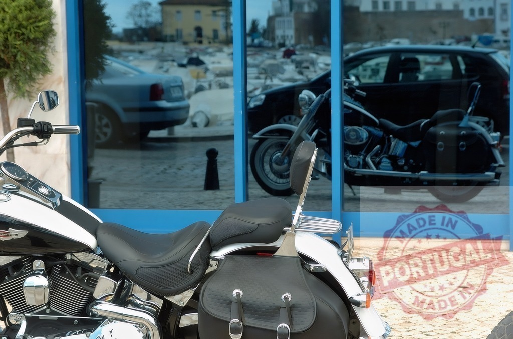 Motorcycle cruiser reflecting in blue shop window on urban street | Classic motorcycle parking on a sidewalk with its reflection visible in a glass window - Realized with Pictrs.com