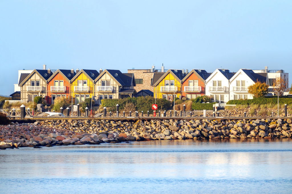 Wandbild: Bunte Ferienwohnungen in Olpenitz  | Dieses Wandbild im Querformat zeigt bunte Ferienwohnungen direkt am Meer in Olpenitz. Auf der Wasserobenfläche ist eine leichte Spiegelung der bunten Ferienwohnungen zu sehen.  - Realisiert mit Pictrs.com