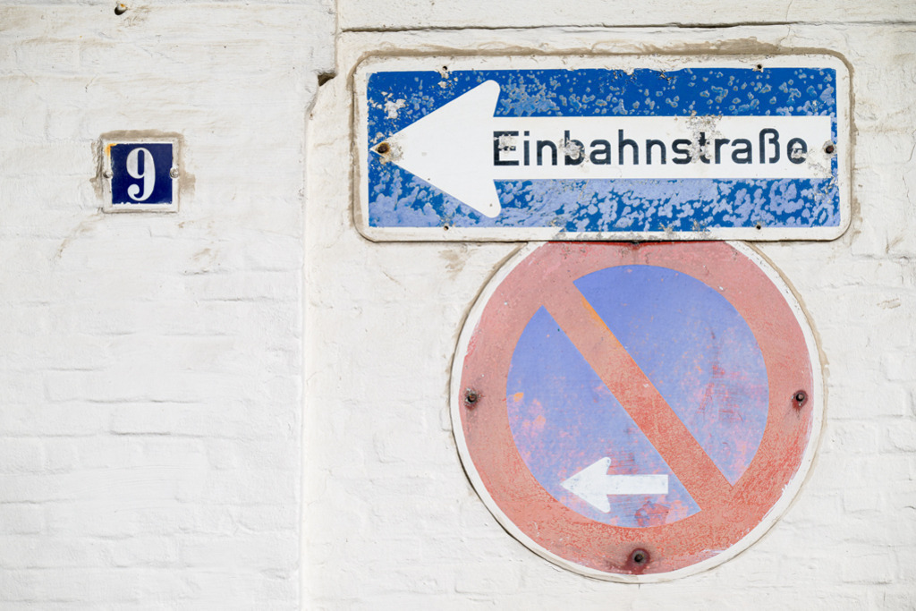 Einbahn PV 9 | Zwei verwitterte Straßenschilder an einer weißen Hausmauer stehen im Kontrast zu dem kleinen blauen Schild, auf dem die 9 als Hausnummer steht. — Auflösung des Originals: 8256 x 5504 px. - Realisiert mit Pictrs.com