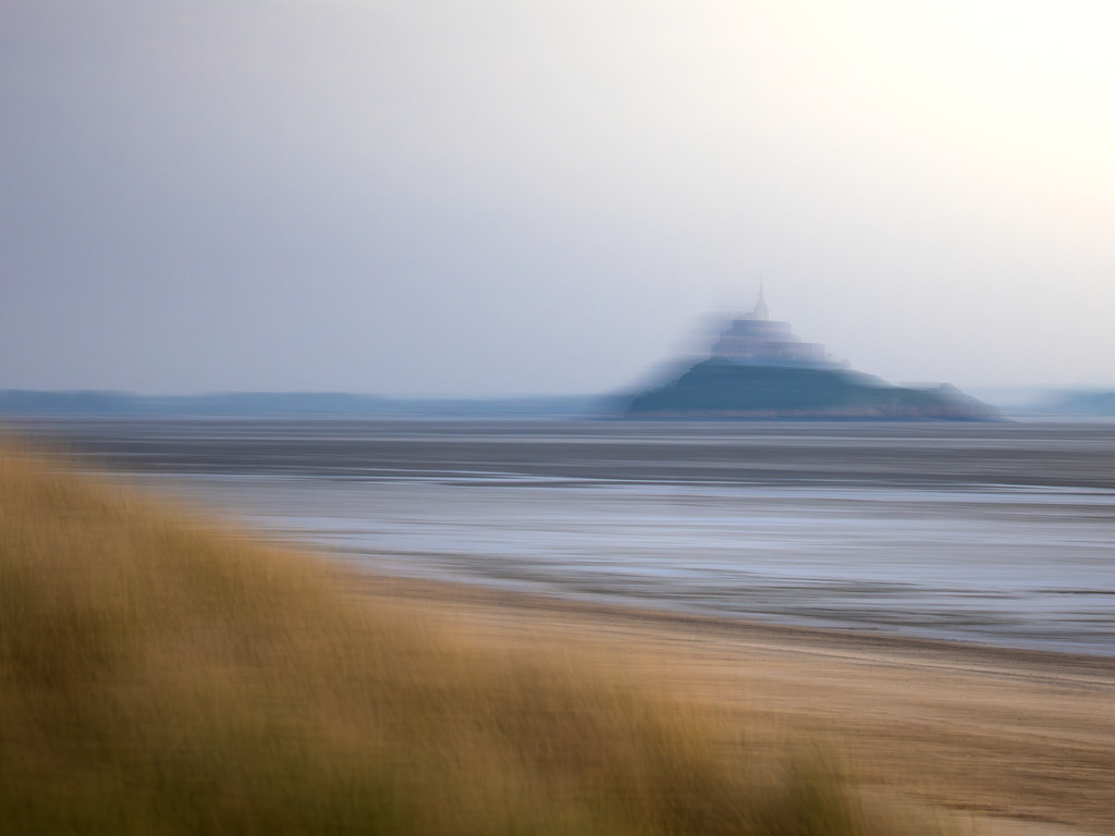 Zwischen den Welten | Wie aus dem Nebel der Erinnerung steigt eine ferne Silhouette empor – einsam, entrückt, fast unwirklich. Ein Hügel, eine Insel, ein uralter Ort, der gleichsam aus dem Meer der Zeit auftaucht. Die Luft scheint zu schweigen, das Licht trägt eine Ahnung von Vergänglichkeit in sich. Dies ist kein Ort, den man betritt – es ist ein Ort, der einen ruft.Ein Ort zwischen Traum und Wachsein.Zwischen Sein und Werden.Ein Sehnsuchtsort der Seele. - Powered by Pictrs.com