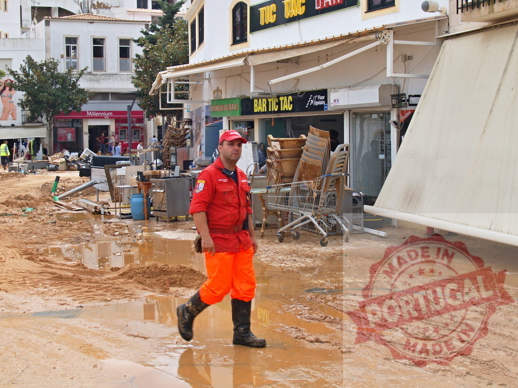 Rescuer walking through a flooded town street cleanup | Albufeira Flood - discruction by weather problems Rescue worker in muddy streets after a natural disaster, cleaning up debris - Realized with Pictrs.com