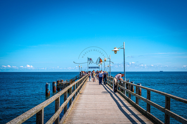 2026-08-08_11-53-50_230 | Ein hölzerner Steg erstreckt sich ins Meer unter einem strahlend blauen Himmel, gesäumt von Menschen, Bansin, Usedom, Mecklenburg-Vorpommern, Deutschland - Realisiert mit Pictrs.com