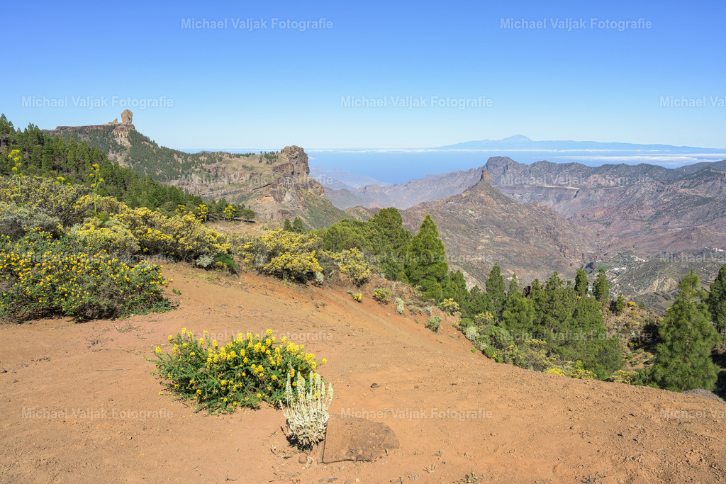 Vista Roque Nublo Gran Canaria | Vom Aussichtspunkt Vista Roque Nublo bietet sich ein weiter Blick über das Zentrum Gran Canarias. Bei klarem Wetter reicht die Sicht bis zur Küste und manchmal sogar bis zum Teide auf Teneriffa. Der Himmel ist wolkenlos, das Licht scharf – jede Kontur der Felslandschaft tritt deutlich hervor. Der Roque Nublo, ein markanter Basaltmonolith, ragt wie ein Wahrzeichen in die Höhe und ist ein beliebtes Ziel für Wanderer. - Realisiert mit Pictrs.com