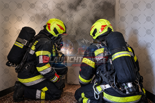 Feuerwehr im Innenangriff – Atemschutztrupp vor verrauchter Tür | Realistisches Symbolbild eines Atemschutztrupps der Feuerwehr, der sich geduckt einer verrauchten Tür nähert. Die Feuerwehrleute sind mit Atemschutzgeräten, Schutzkleidung und Helmen ausgestattet und bereiten sich auf den Innenangriff vor. Das Bild eignet sich für Print- und Onlinemedien, Zeitungsberichte, Feuerwehrberichte sowie Beiträge über Brandeinsätze, Atemschutz und Brandbekämpfung. - Realisiert mit Pictrs.com