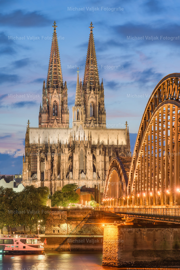 Beleuchteter Kölner Dom am Abend | Der Kölner Dom, eines der großartigsten Beispiele gotischer Architektur, erstrahlt am Abend in einem ganz besonderen Licht. Wenn die Sonne untergeht, wird die Kathedrale mit einem kunstvollen Beleuchtungssystem in Szene gesetzt, das ihre filigranen Steinmetzarbeiten und die majestätischen Türme hervorhebt. Dieses Schauspiel der Lichter zieht nicht nur Touristen aus aller Welt an, sondern ist auch ein Symbol der Stadt Köln und ihrer reichen Geschichte. Die abendliche Beleuchtung des Doms bietet einen atemberaubenden Anblick und ist ein Zeugnis menschlicher Kunstfertigkeit und Ingenieurskunst. - Realisiert mit Pictrs.com