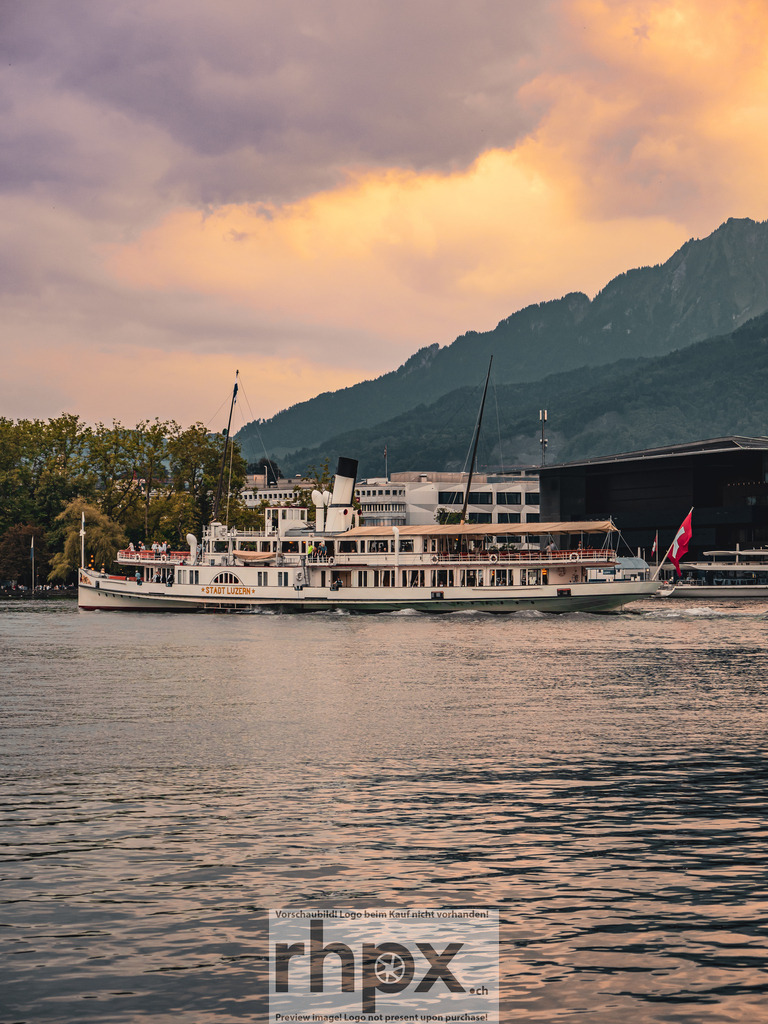 Dampfschiff Stadt Luzern bei Sonnenuntergang | p><strong>Tradition. Wasser. Goldstunde.</strong><p>Das Flaggschiff Stadt Luzern gleitet sanft über den Vierwaldstättersee, während das warme Abendlicht die Berge in sanfte Pastelltöne taucht. Diese Aufnahme fängt die zeitlose Eleganz der Schweizer Schifffahrt vor der markanten Kulisse des Pilatus ein.</p> - Realisiert mit Pictrs.com