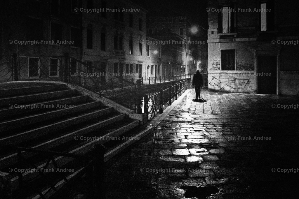 Nacht in Venedig | Ein Mann geht allein durch die beleuchtete Altstadt von Venedig in der Nacht. Straßenfotografie aus Italien in schwarz und weiß. - Realisiert mit Pictrs.com