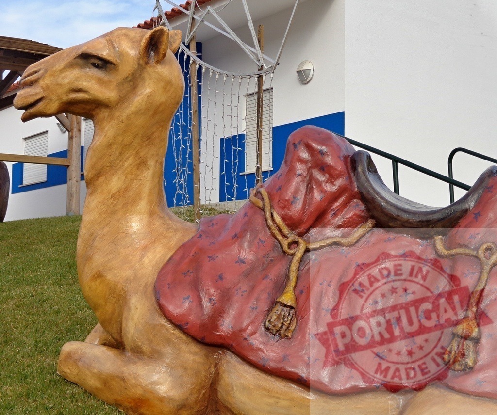 Resting camel statue with red saddle blanket in christmas setting | Camel statue resting on grass with red saddle blanket in christmas setting - Realized with Pictrs.com