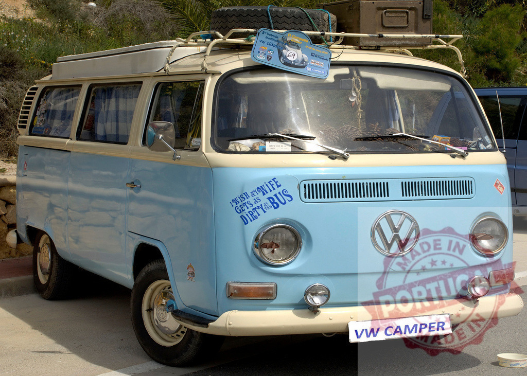 Light blue and cream Volkswagen camper van parked in a parking lot | Classic Volkswagen camper van parked, showing a funny sticker on the front - Realized with Pictrs.com