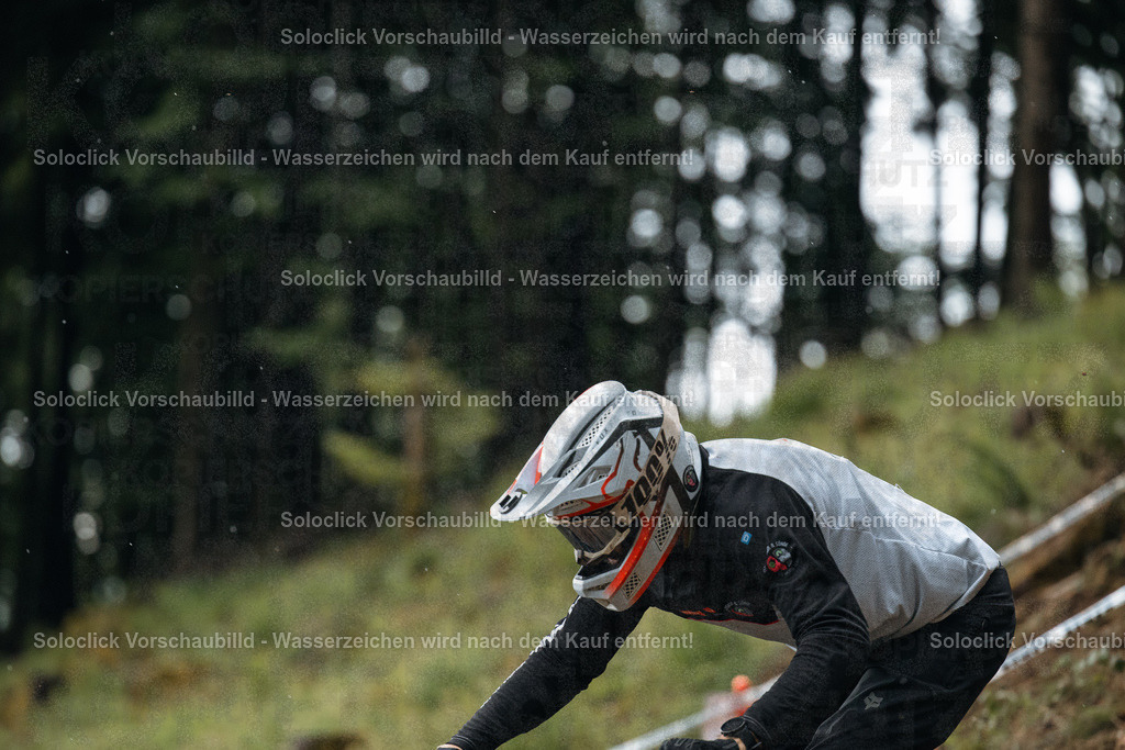 Mountainbike-Abenteuer im Wald | Das Bild zeigt einen Mountainbiker in voller Ausrüstung, der einen steilen, schlammigen Weg in einem bewaldeten Gebiet hinunterfährt. Der Fokus liegt auf dem Fahrer, der in einer dynamischen Pose zu sehen ist, während er den Weg bewältigt. Die Umgebung besteht aus dichtem Grün und Bäumen, was eine natürliche und herausfordernde Umgebung schafft. - Realisiert mit Pictrs.com