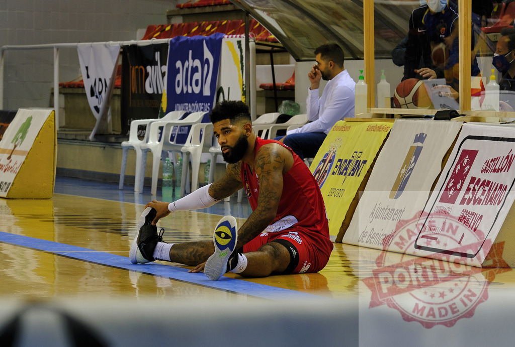 Basketball player stretching on court before game | Athlete sitting on gym floor stretching leg muscles before a sport event - Realisiert mit Pictrs.com