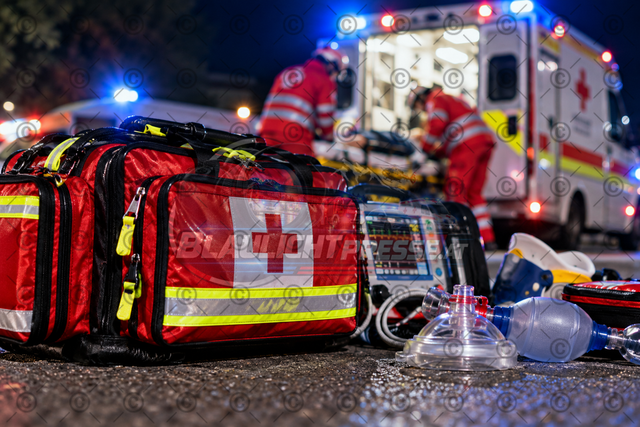 Symbolbild Rotes Kreuz – Notarzttasche und medizinische Ausrüstung bei einem Rettungseinsatz | Realistisches Symbolbild eines Rettungseinsatzes mit Notarzttasche und medizinischer Ausrüstung im Vordergrund. Im Hintergrund sind Sanitäter bei der Versorgung eines Patienten neben einem Rettungswagen mit eingeschalteter Einsatzbeleuchtung zu sehen.Das Bild eignet sich für Print- und Onlinemedien zur Berichterstattung über Rettungseinsätze, Notarztversorgung, Erste Hilfe, medizinische Notfälle und den Rettungsdienst. - Realisiert mit Pictrs.com