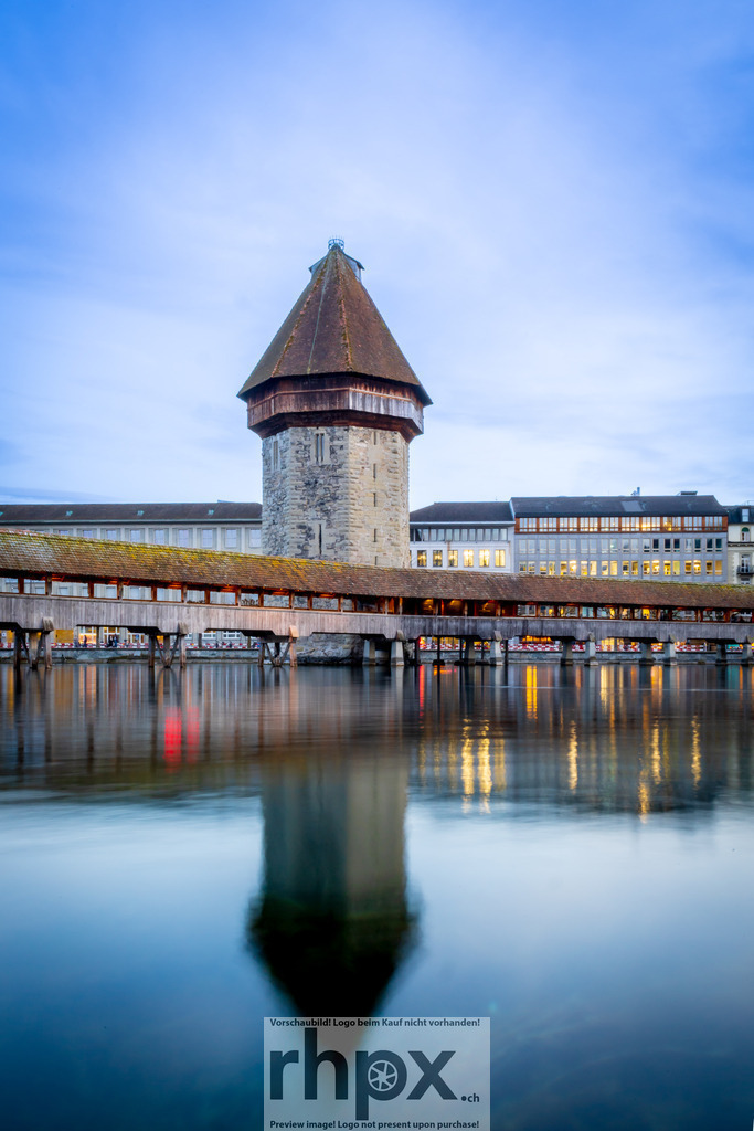 Kapellbrücke und Wasserturm Luzern bei Dämmerung | Spiegelung. Stein. Stille.Die sanfte Spiegelung des historischen Wasserturms im ruhigen Flussbett der Reuss erzeugt eine fast magische Symmetrie. Das warme Licht der Brücke bildet zur blauen Stunde einen fesselnden Kontrast zum kühlen Stein dieses Wahrzeichens.Wähle unter "Produktauswahl" dein Wunschformat: Vom klassischen Wandbild über Puzzle &amp; Tassen bis zum digitalen Download (z.B. als Handy-Hintergrund). - Realisiert mit Pictrs.com