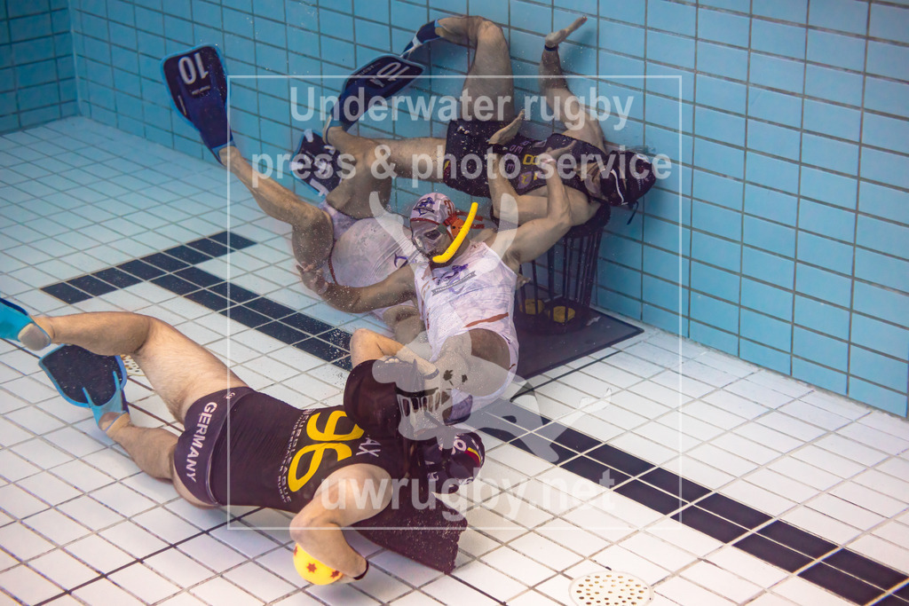 24. - 26.11.2023: Unterwasser-Rugby Champions Cup 2023  | DUC Krefeld (Deutschland) in blau gegen NJ Hammerheads (USA) in weiß.  Der Krefelder Max Keiten (blau #96) greift das Tor der New Jersey Hammerheads an, währendessen hat Jannik Graf (blau #8) den gegenerischen Torwart abgelöst und hindert den Torwart wieder sein Tor zu verteidigen. - Realisiert mit Pictrs.com