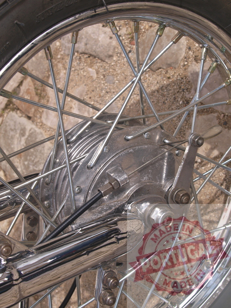 Motorcycle vintage wheel spokes and brake close up | Vintage motorcycle wheel featuring chrome spokes, drum brake, and hub on pavement background - Realized with Pictrs.com