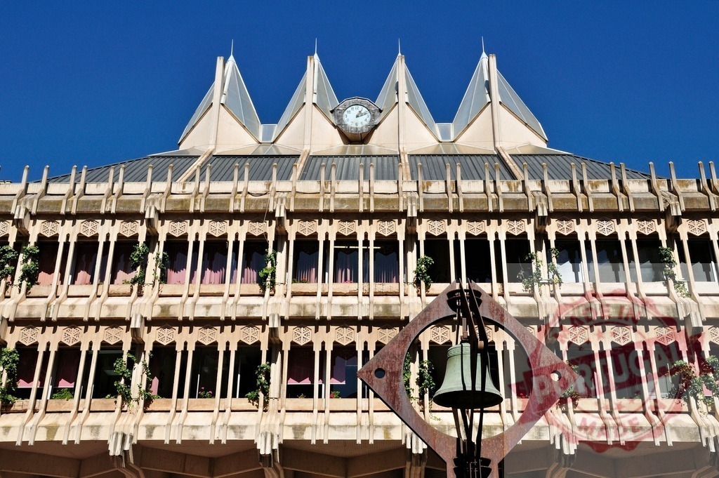 Castilla-La Mancha University building facade with modern clock and abstract bell sculpture. Extremdura - Spain | Exterior view of the university building featuring a roof clock and a contemporary bell art piece - Realisiert mit Pictrs.com