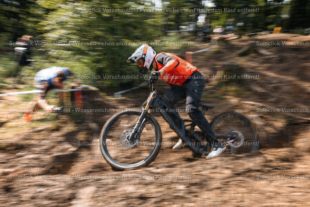 Adrenalin im Wald | Ein Mountainbiker in voller Montur rast mit hoher Geschwindigkeit durch einen verschneiten Wald. Die Bewegung des Fahrers und des Fahrrads wird durch die lange Belichtungszeit dargestellt, was zu einem verschwommenen Effekt führt. Der Fahrer trägt einen orangefarbenen Helm und eine Jacke, sowie schwarze Handschuhe und Hosen. Das Fahrrad ist ein Downhill-Mountainbike mit dicken Reifen und einer robusten Federgabel. Der Hintergrund besteht aus Bäumen und Unterholz, die ebenfalls verschwommen sind. - Realisiert mit Pictrs.com