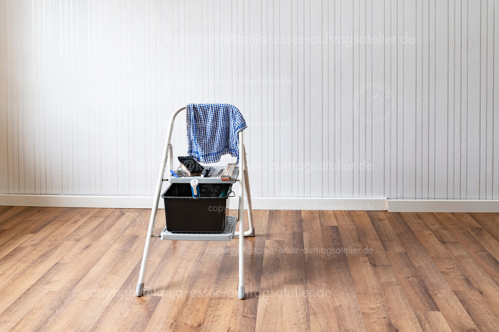 Frisch tapezierte Zimmerwand mit Arbeitsgeräten im Vordergrund. | Ein Raum wurde renoviert. Tapezier Utensilien liegen auf einer Leiter. Die Wand hat eine neue gestreifte weiße Tapete. Fußleisten wurden gelöst. Copy Space.
