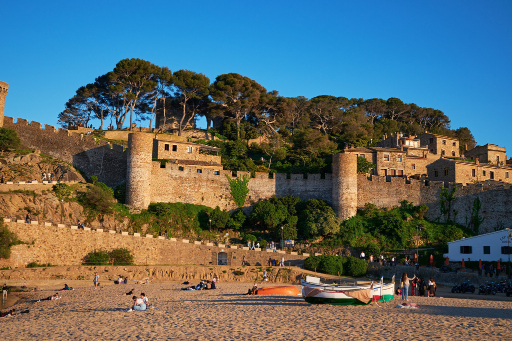 Blick über den Strand auf die Vila Vella | Tossa de Mare, Frankreich - May 11, 2024: Blick über den Strand auf die Vila Vella mit blauem Himmel und Booten im Vordergrund. - Realisiert mit Pictrs.com