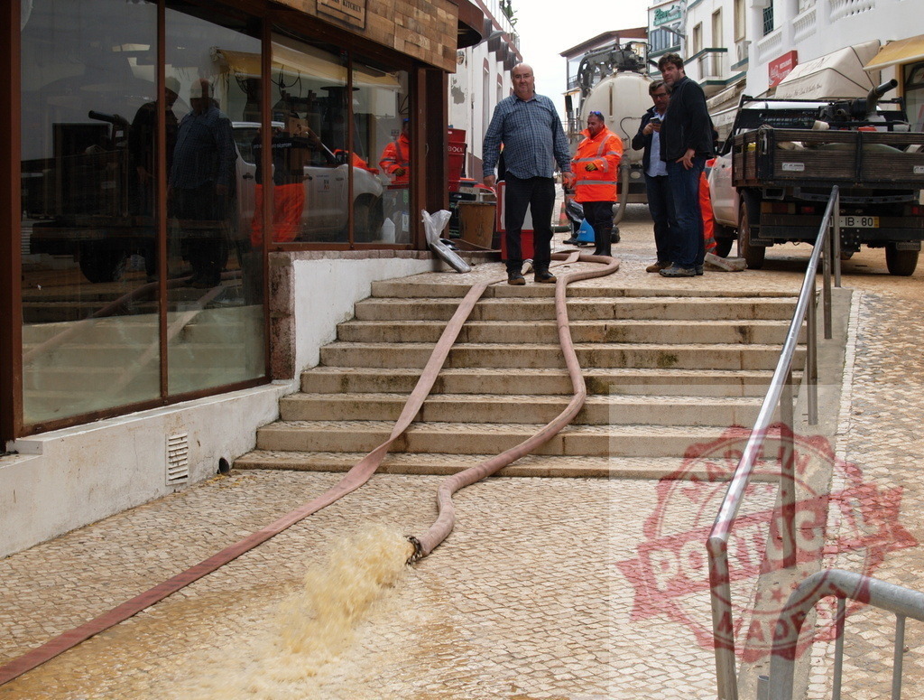 Workers pumping floodwater from street after emergency | Albufeira Flood - discruction by weather problems Emergency workers using a pump to remove muddy floodwater from a street - Realisiert mit Pictrs.com